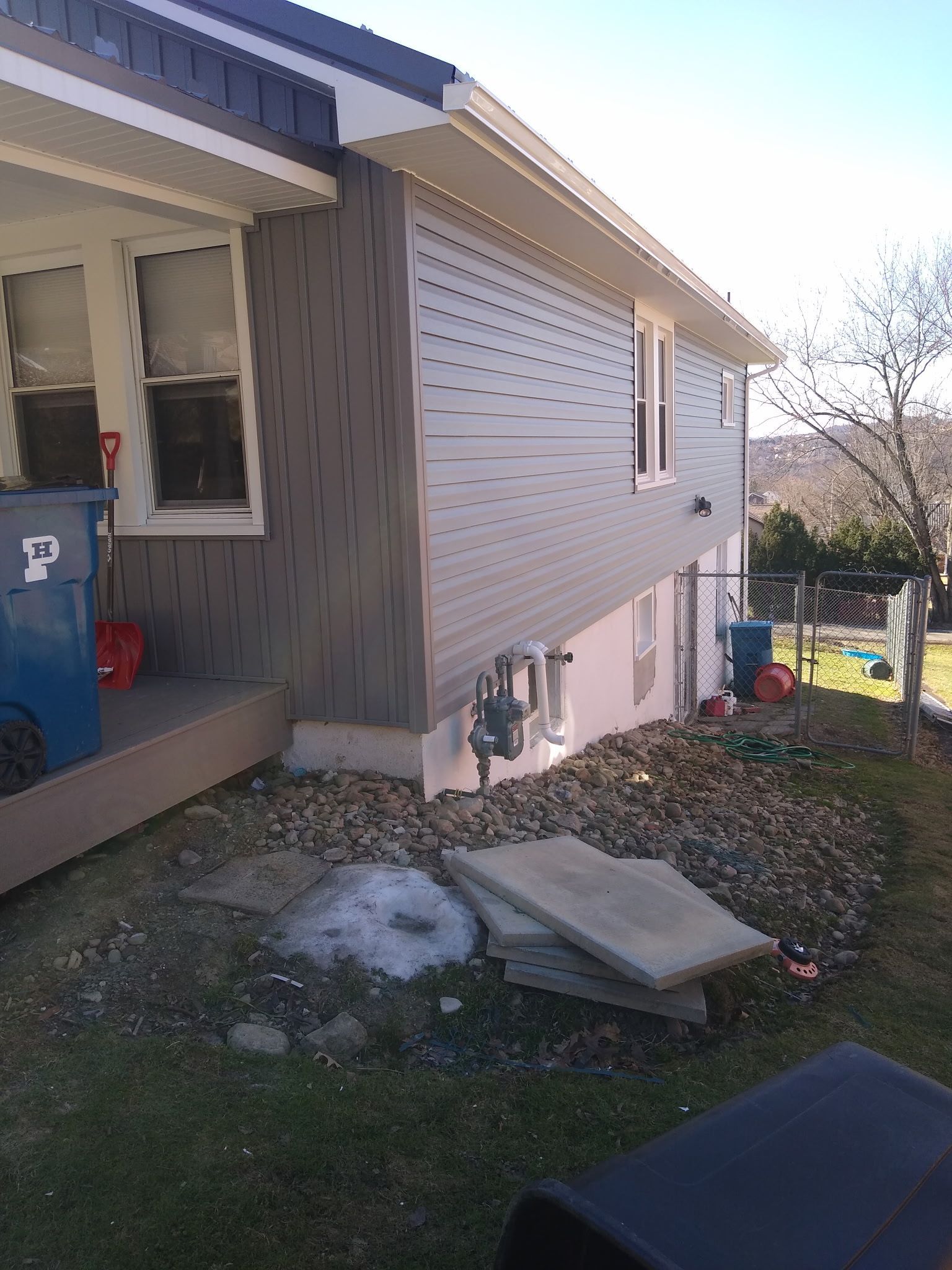 The side of a house with a blue trash can with the letter p on it.