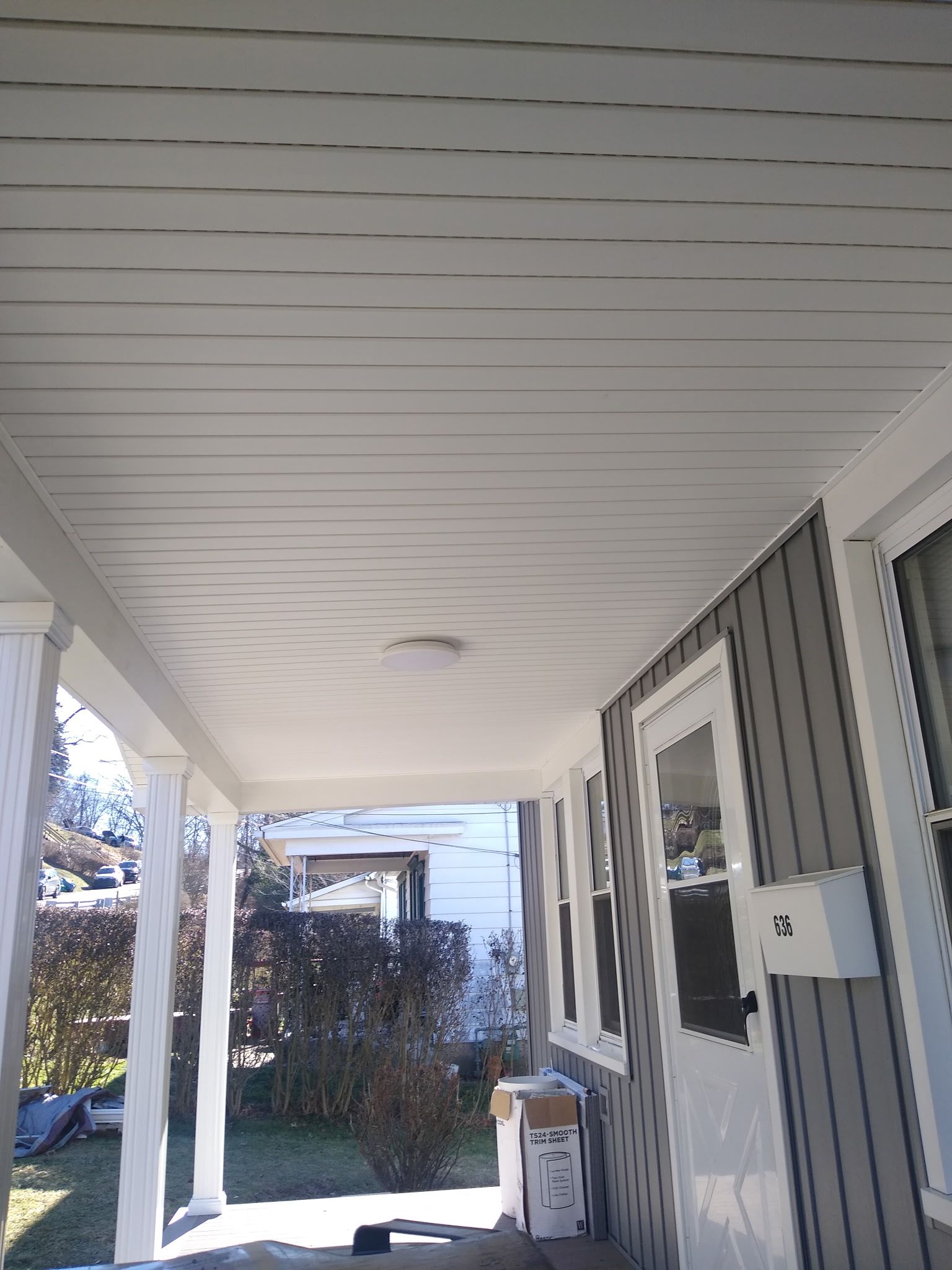 A porch with a white ceiling and a white door on a house.