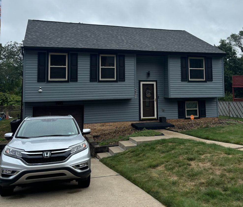 A silver honda cr v is parked in front of a gray house with black shutters.