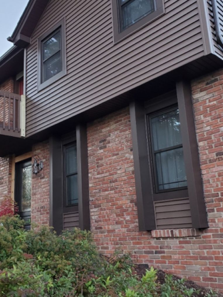 A brick house with brown siding and black windows.