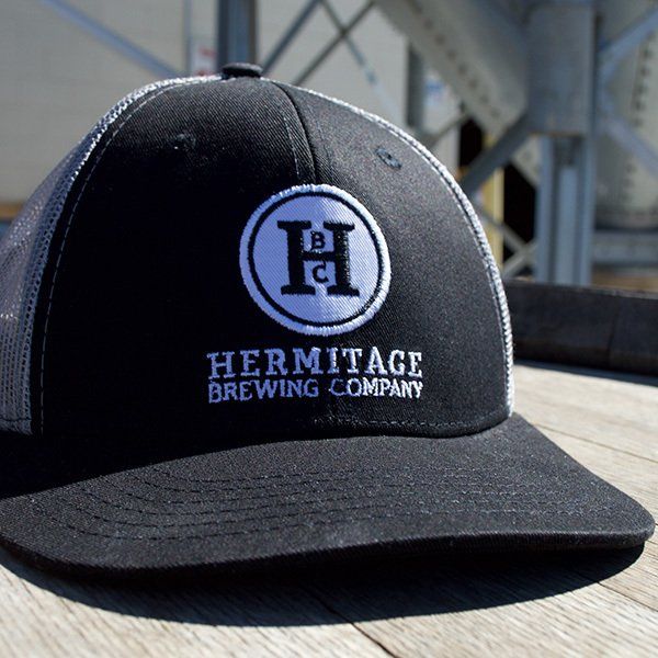 A black hermitage brewing company hat sits on a wooden table