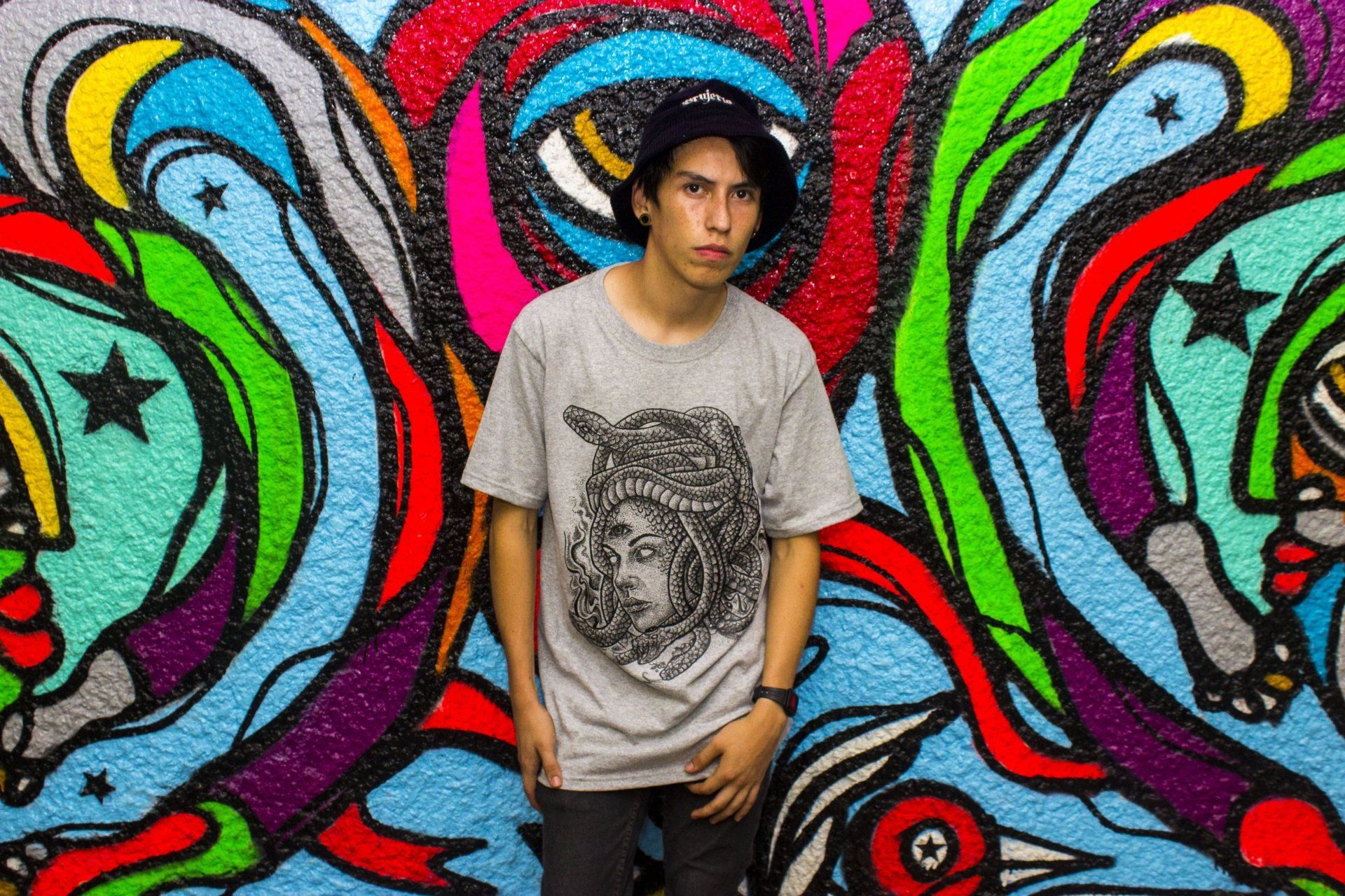 A young man is standing in front of a colorful graffiti wall.