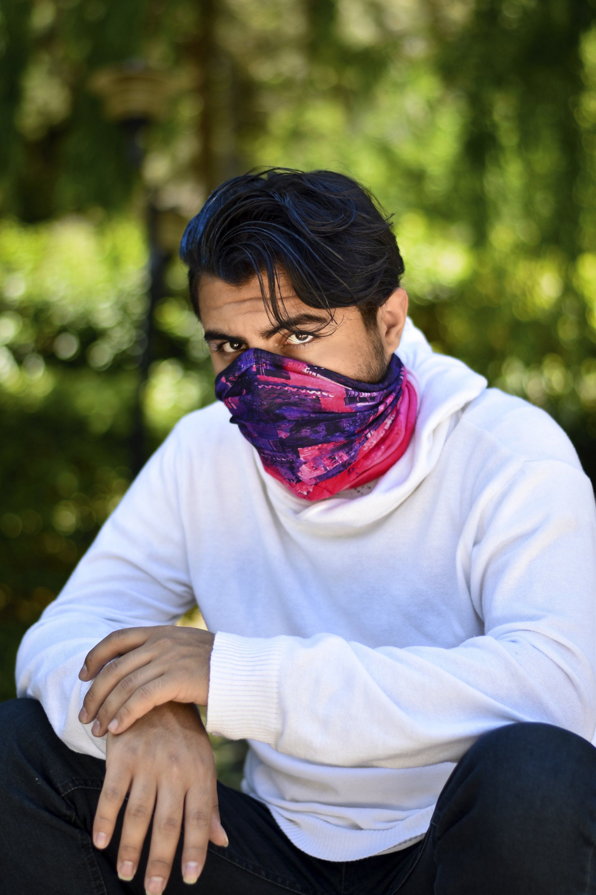 A man wearing a bandana around his neck is sitting on the ground.