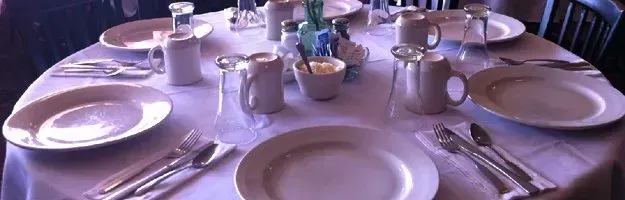 A table set with plates, silverware, cups, and creamers for a meal in a restaurant.