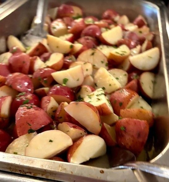 A metal serving tray filled with roasted red potatoes seasoned with green herbs.