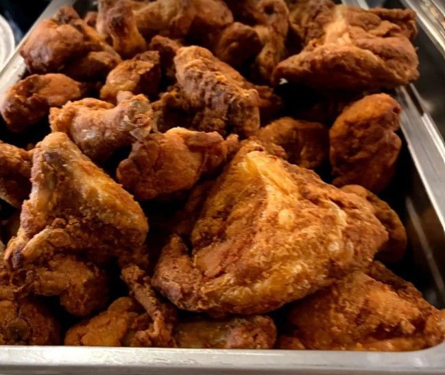 A metal tray filled with freshly fried, golden-brown chicken pieces.