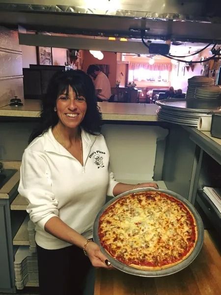 Woman holding pizza in a restaurant kitchen, smiling.