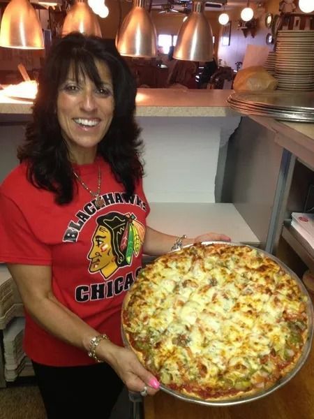 Woman in Blackhawks shirt holding a large pizza in a restaurant.