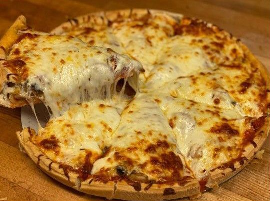 A cheesy, baked pizza on a wooden surface with a slice being lifted, showing melted, stretching mozzarella.