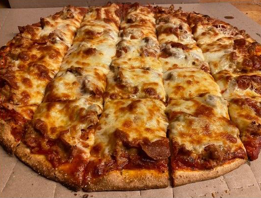 A round, cheesy pizza sits on a wooden surface with one slice being lifted, showing melted cheese pulling away.