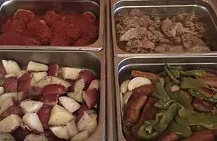 Four metal food trays: seasoned meat, cooked meat chunks, potatoes, and sausage with vegetables.
