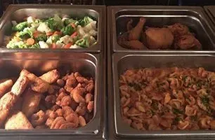 Buffet with four stainless steel food trays: vegetables, chicken, fried items, and pasta.