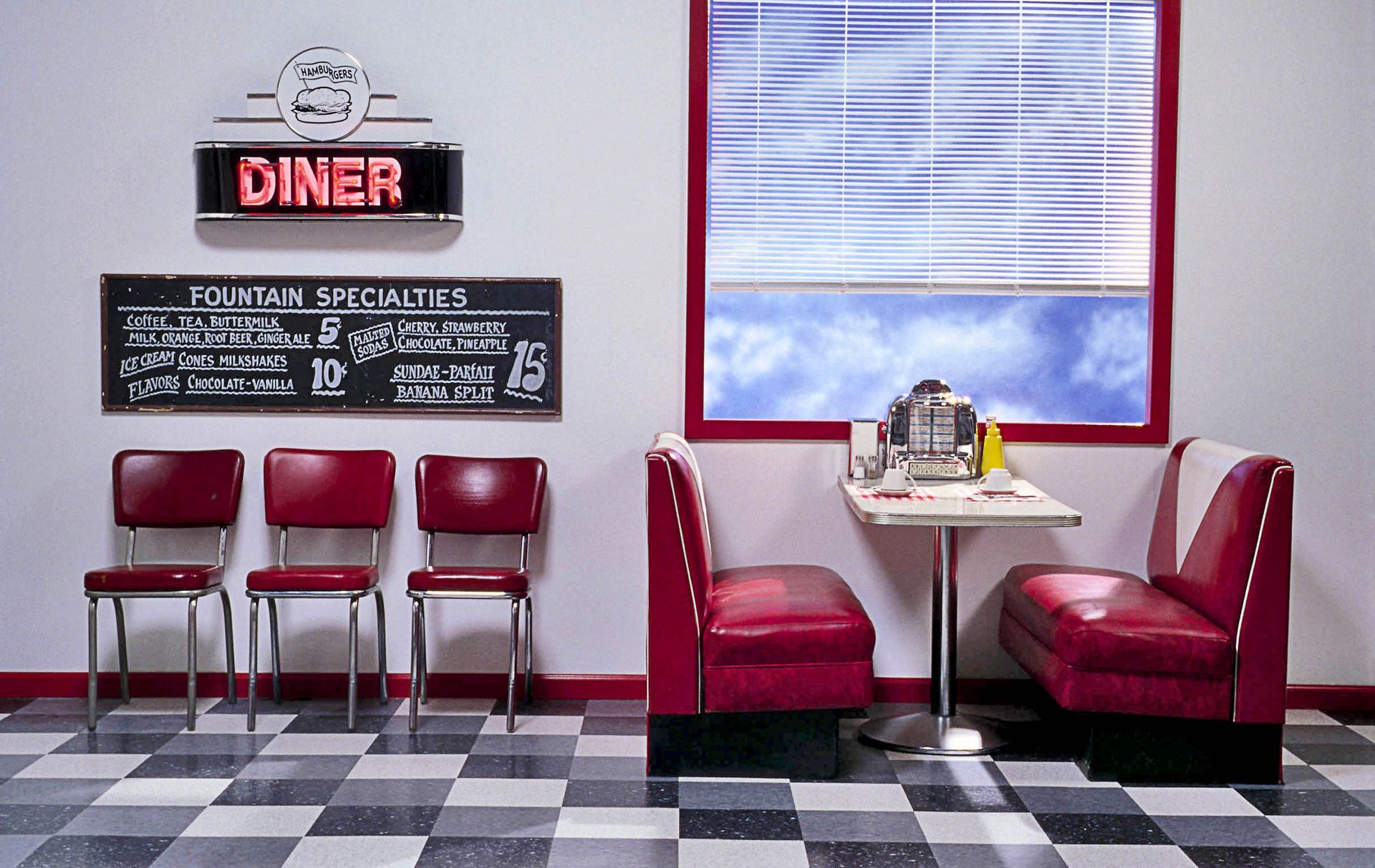 Retro diner interior with red booths, chairs, and neon sign. Black and white checkered floor, window with a blue sky.