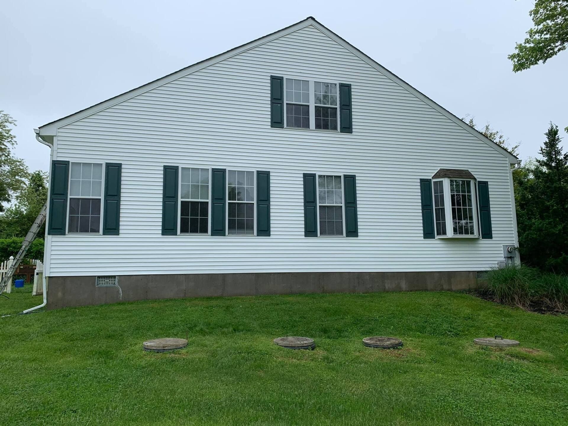 White house with green shutters, gray foundation, and a small bay window.