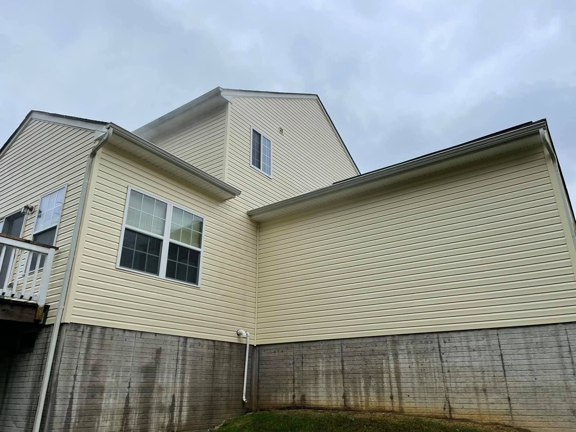 Beige siding on a two-story house with a brick foundation, under a cloudy sky.