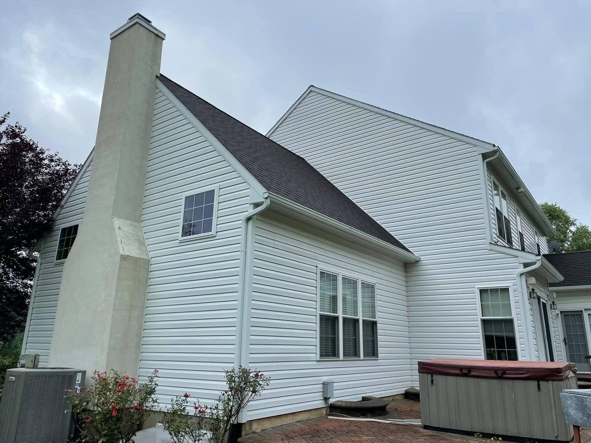 White-sided house with a dark roof and a tall chimney, cloudy sky overhead.