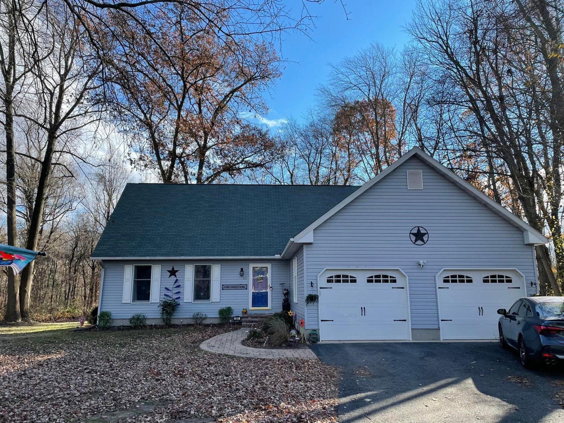 A light blue house with a green roof, two-car garage, and driveway under a blue sky.