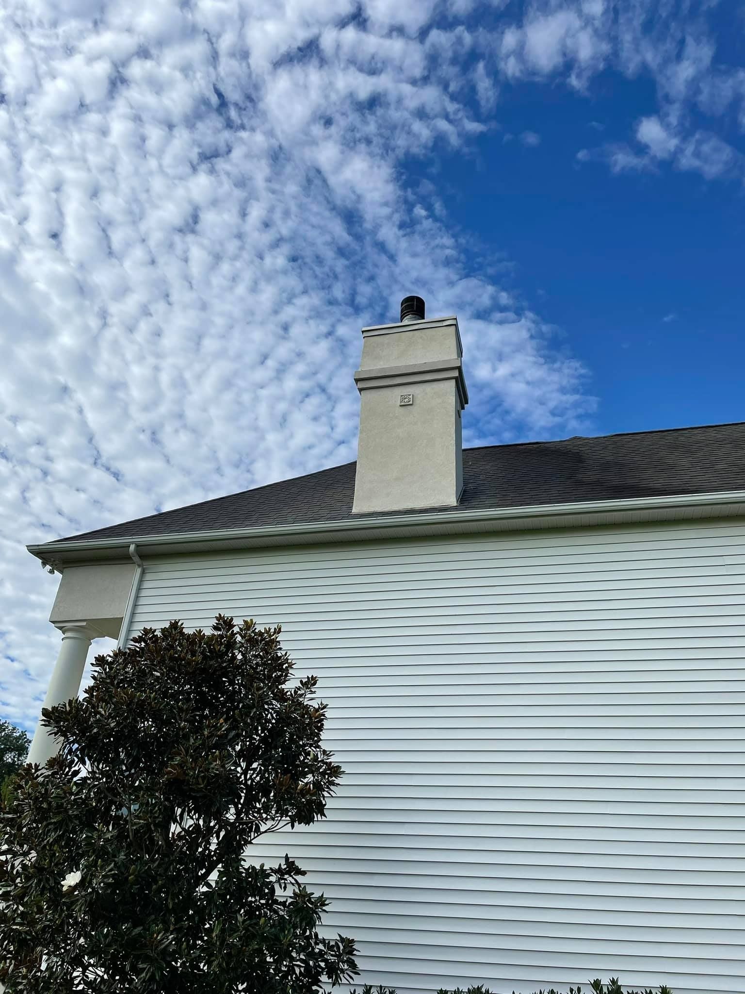 White house exterior with chimney against a blue sky with clouds, tree in the foreground.