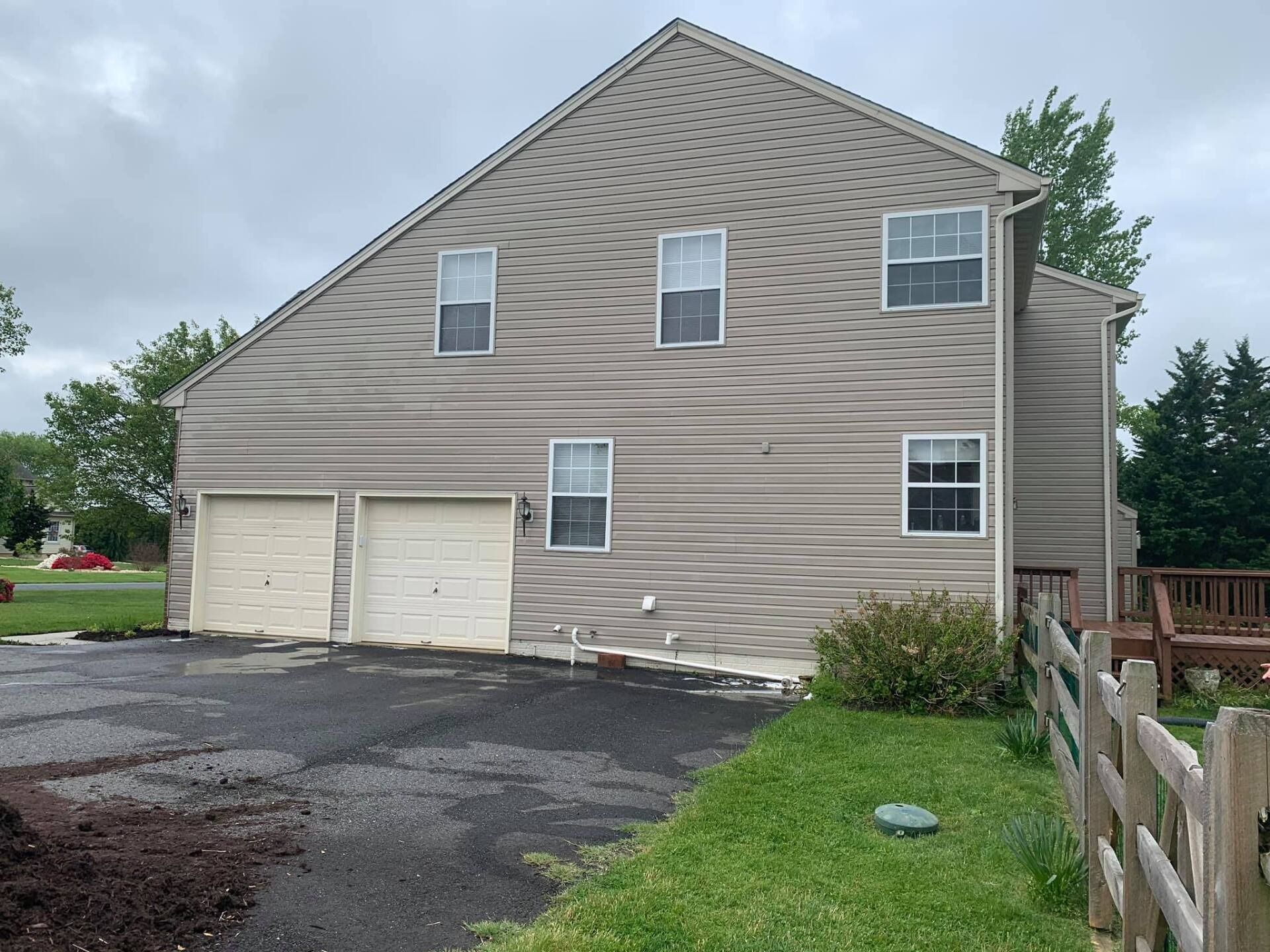 Two-story house with tan siding, two garage doors, and a driveway.