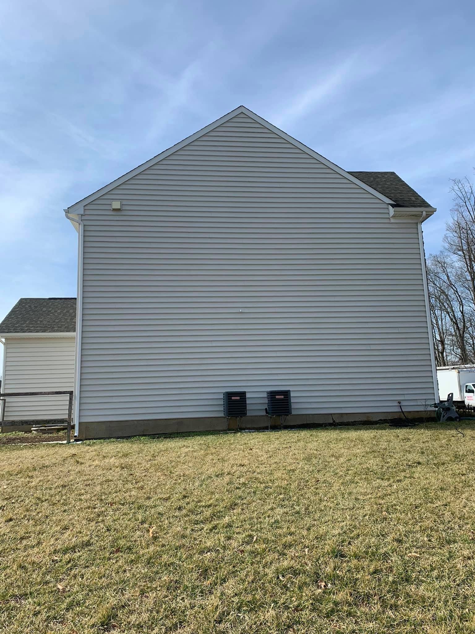 Side of a two-story house with gray vinyl siding, two HVAC units, and a grassy yard under a blue sky.