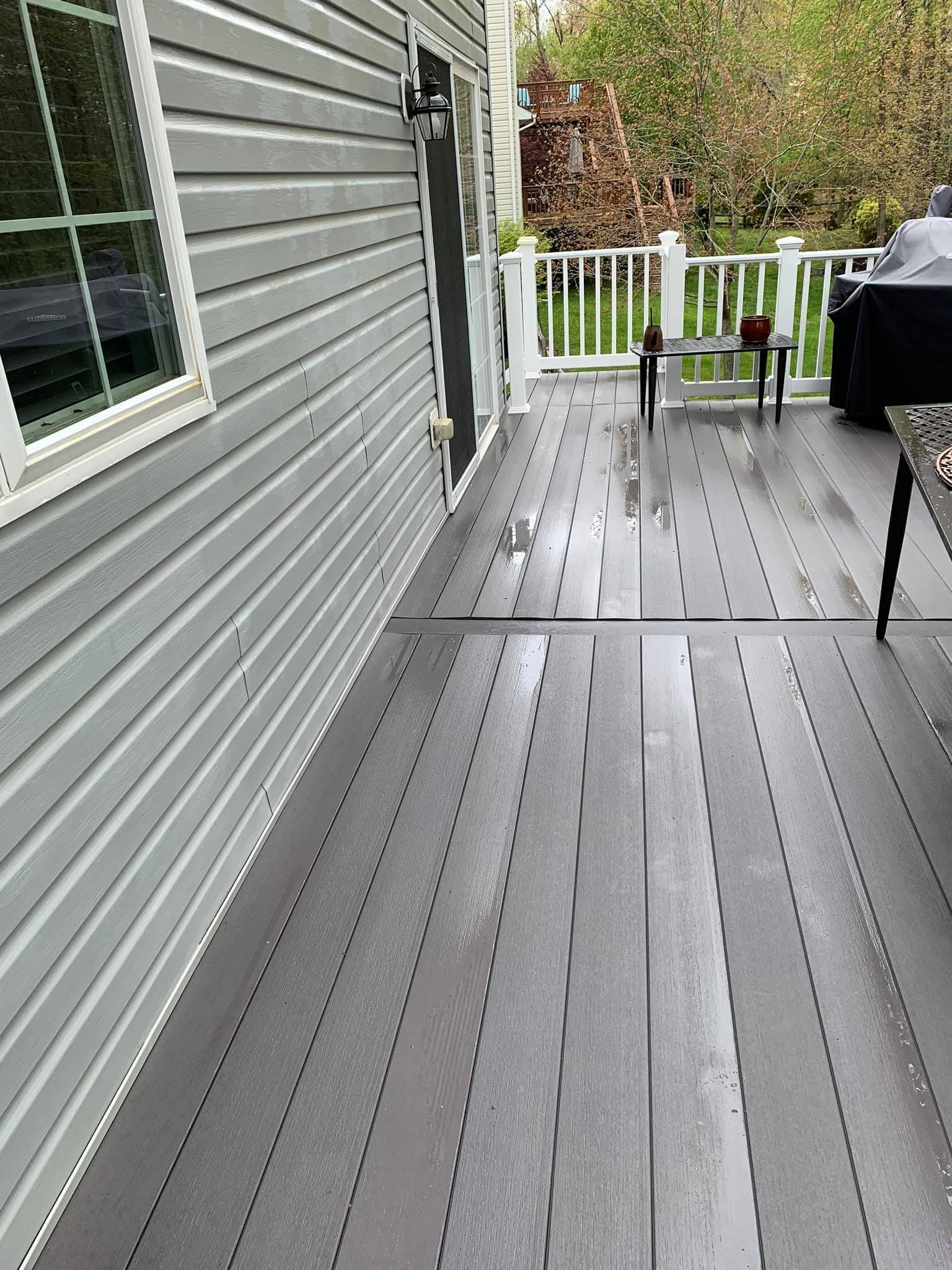 Gray composite deck with a wet surface next to a gray house, white railing, and a black grill.