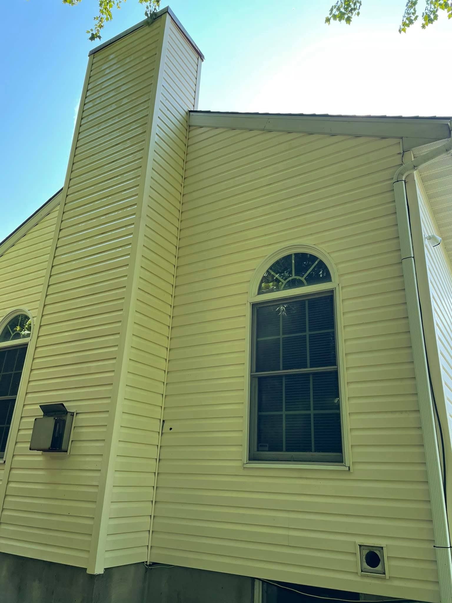 Tan house exterior with chimney, arched window, and blue sky.