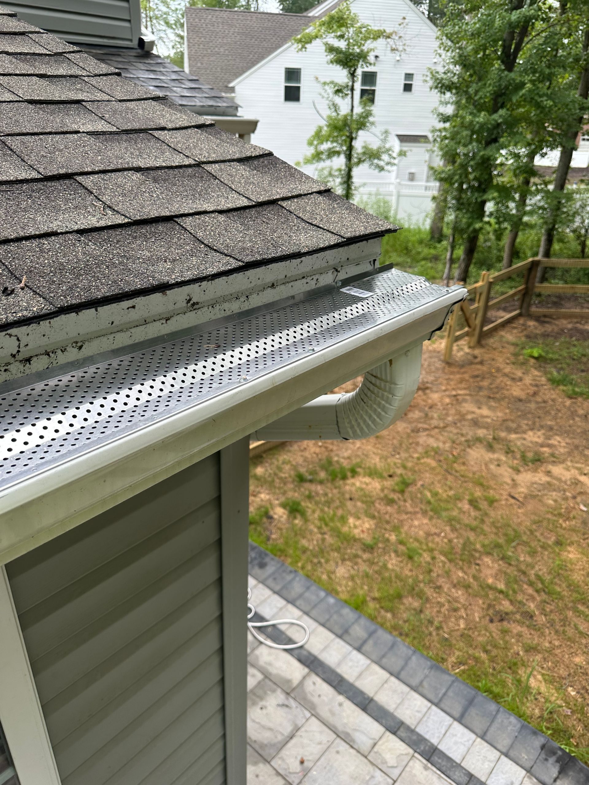 Gutter with mesh cover on a house with gray shingles. A downspout is visible.