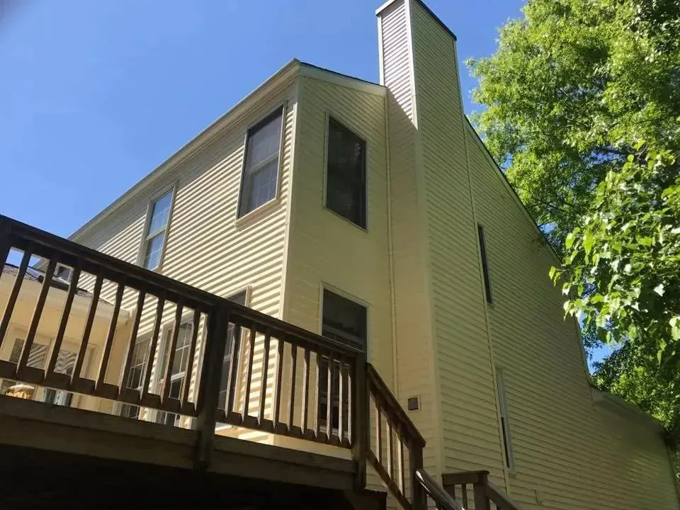 Two-story house with beige siding, brown roof, and brick facade on the right side, set on a green lawn.