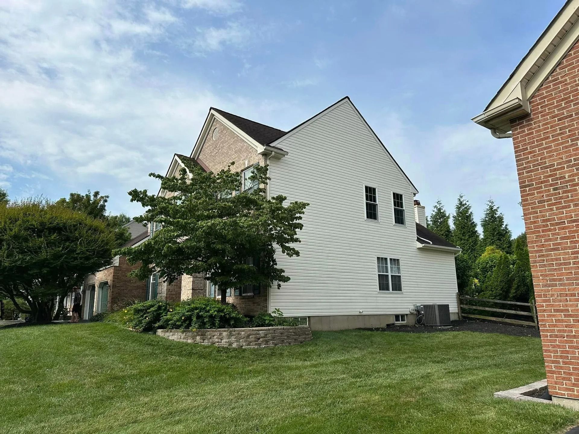 Two-story house with brick and white siding, green lawn, and blue sky.