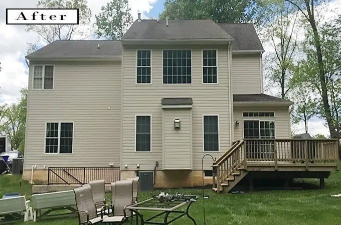 Rear view of a beige two-story house with a wooden deck and backyard. The sky is overcast.
