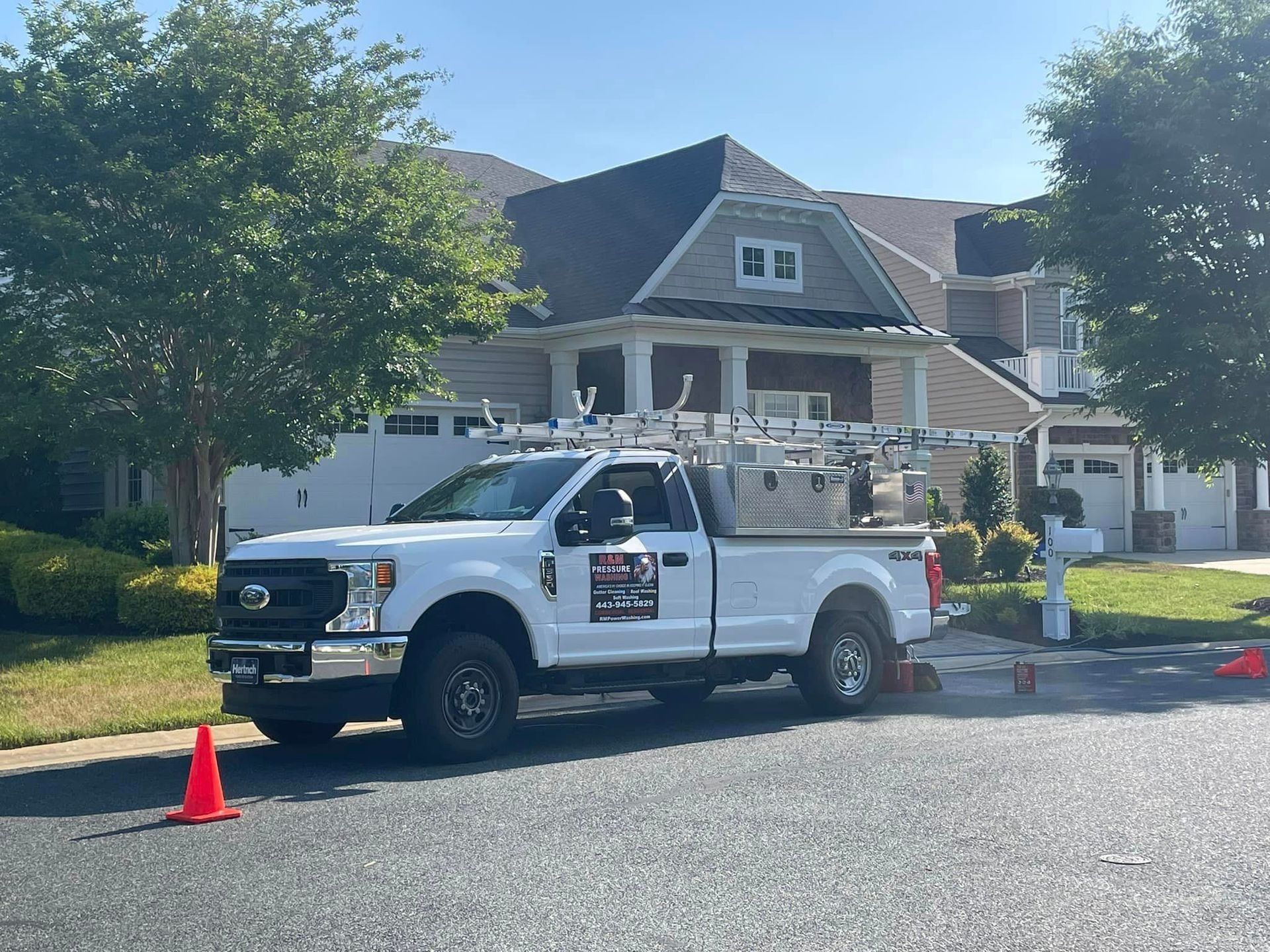 White work truck with ladder on top parked in front of a house. Orange traffic cone in the foreground.