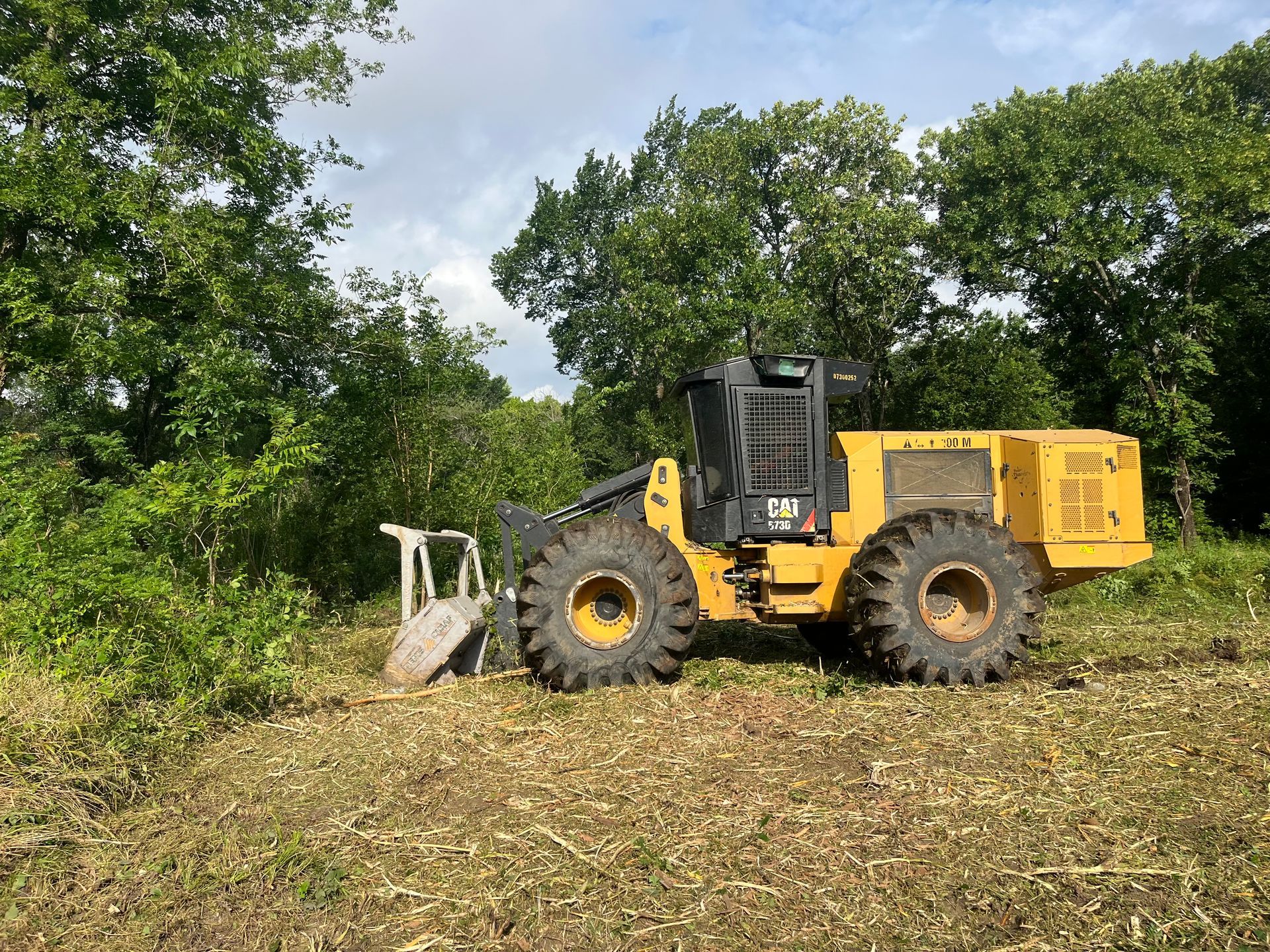 A yellow tractor is parked in a field with trees in the background.