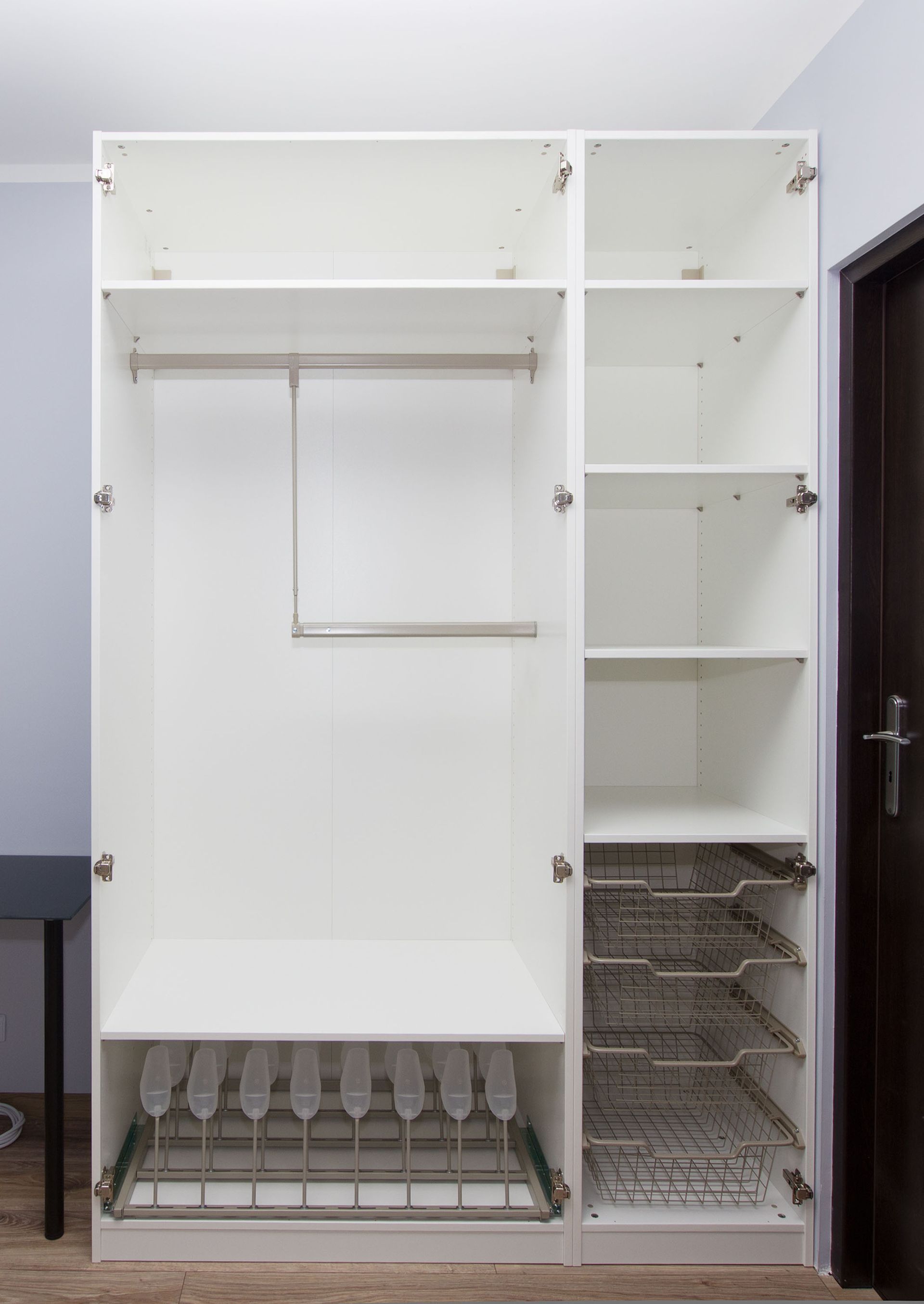 White built-in wardrobe with open doors, featuring a hanging rod, shelves, and wire baskets for storage.