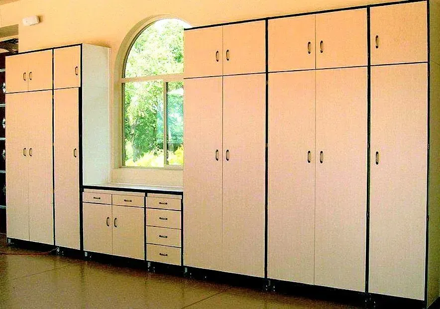 White storage cabinets against a wall, near a window. The cabinets have black frames and gold handles.