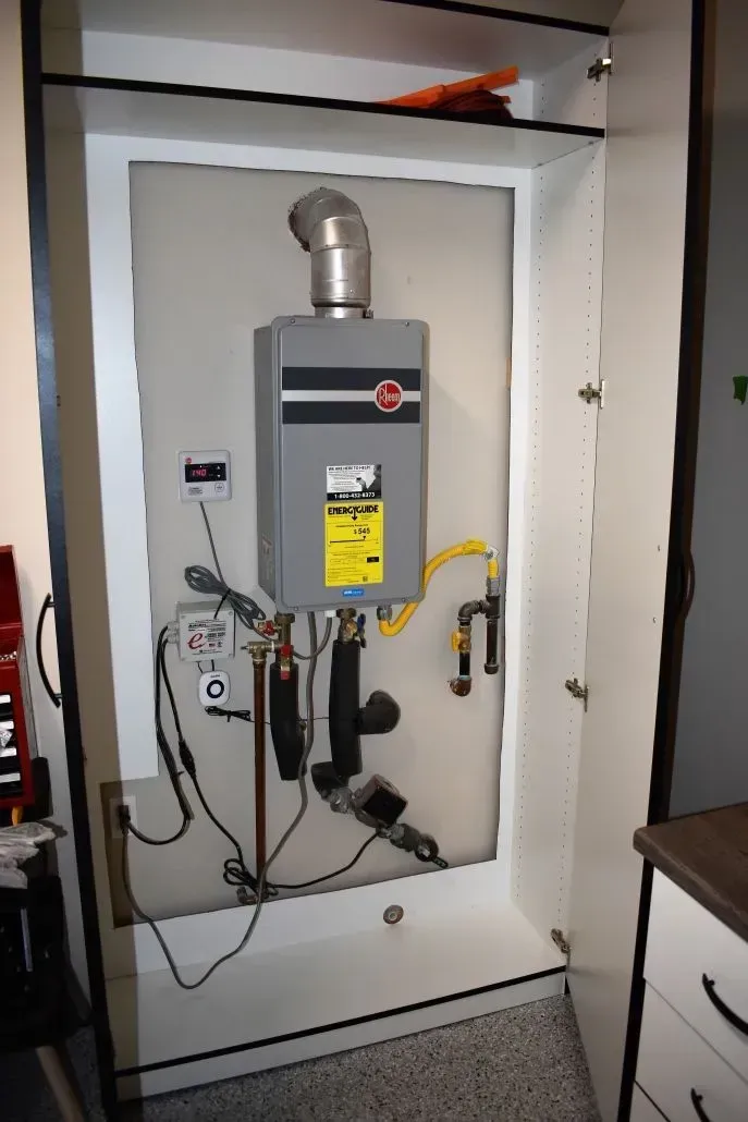 Rheem tankless water heater installed in a cabinet, with attached pipes, wiring, and exhaust vent.