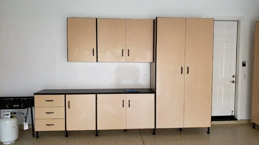 Garage cabinets with overhead and base units; beige doors, black frames; on concrete floor.