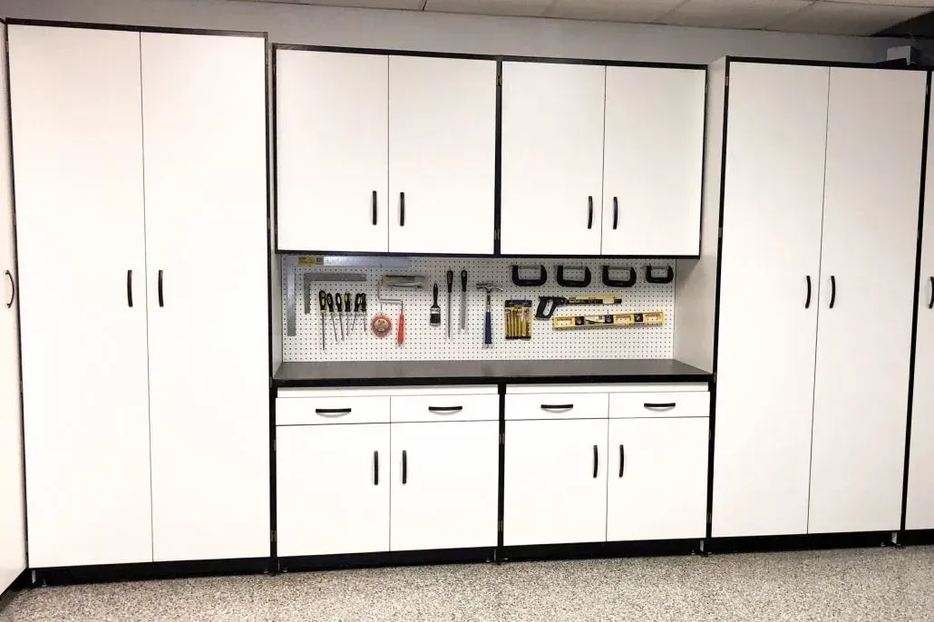 White garage cabinets with black trim and countertop, tools on a pegboard.