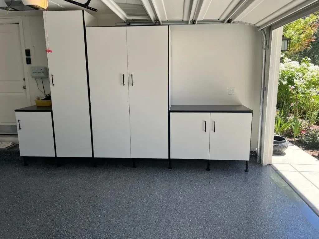 White storage cabinets with black tops and black legs in a garage with a speckled gray floor.