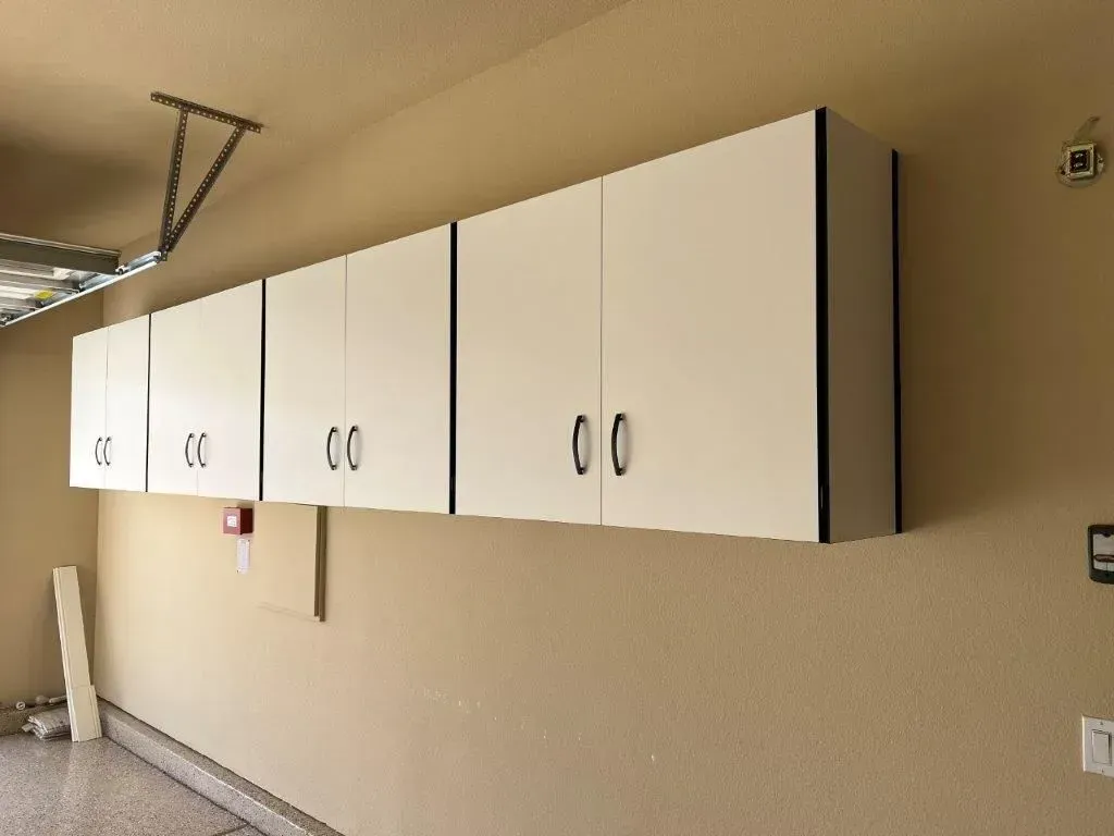 White cabinets with black trim mounted on a tan wall in a garage.