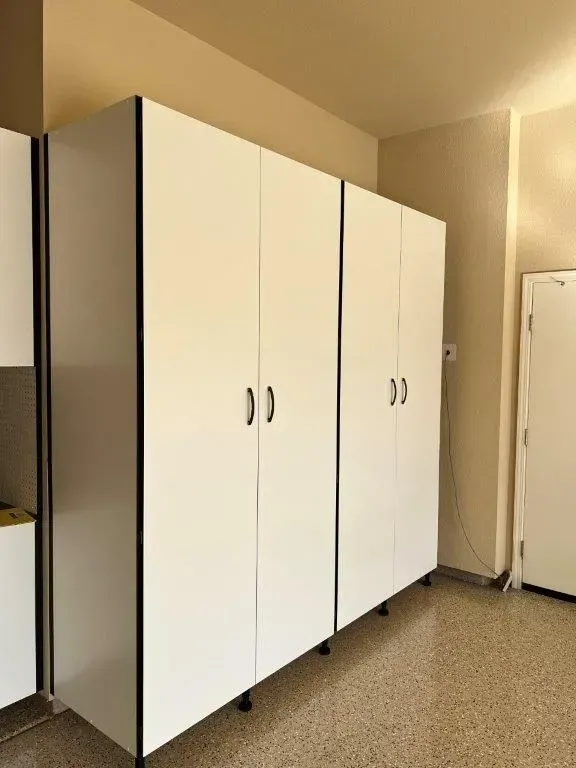 White storage cabinets with black trim in a room with a speckled floor and tan walls.