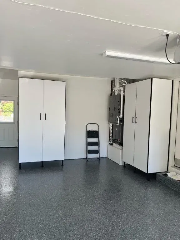 Garage interior with white cabinets, gray floor, and a small ladder.