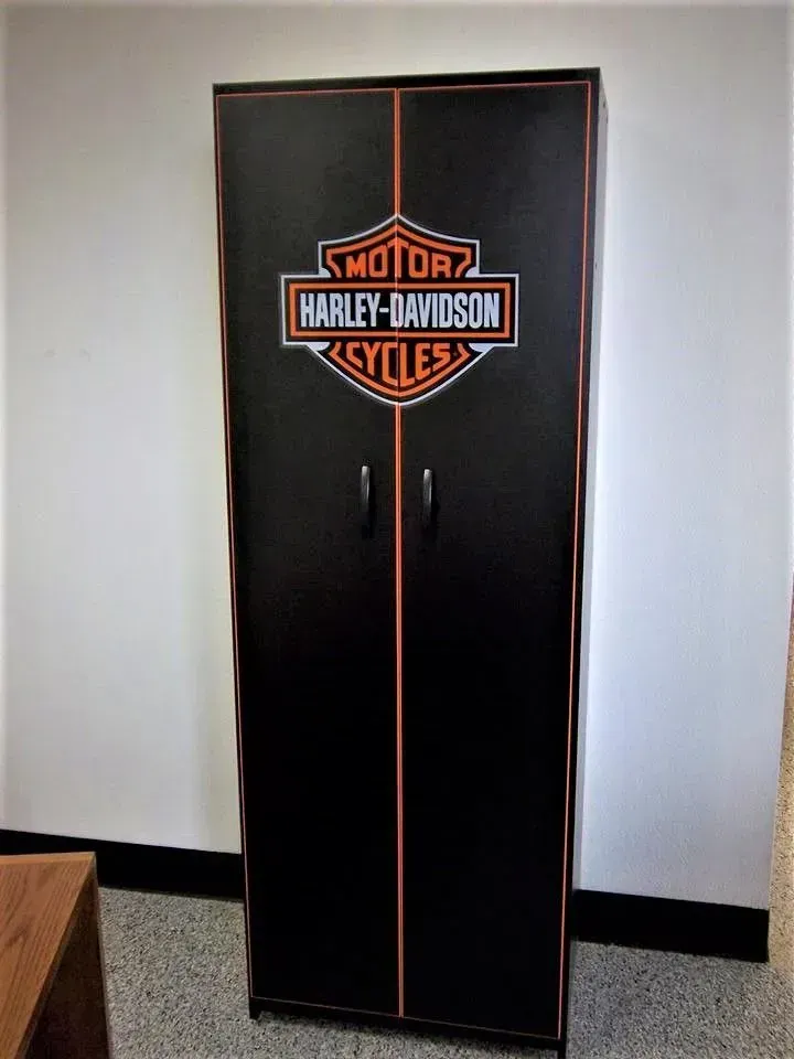 Black Harley-Davidson cabinet with orange trim and logo, two doors, standing against a white wall.