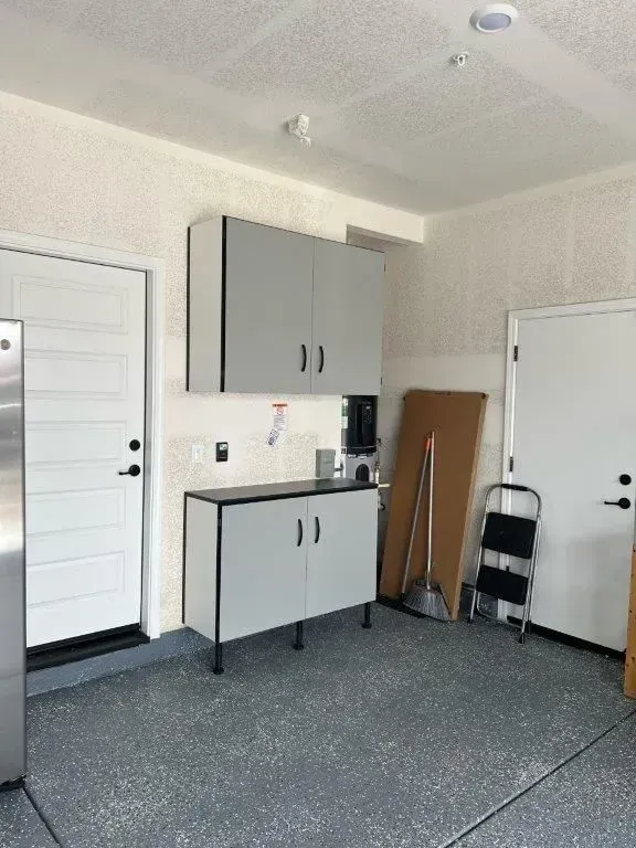 Garage with gray cabinets, white doors, and a speckled floor.