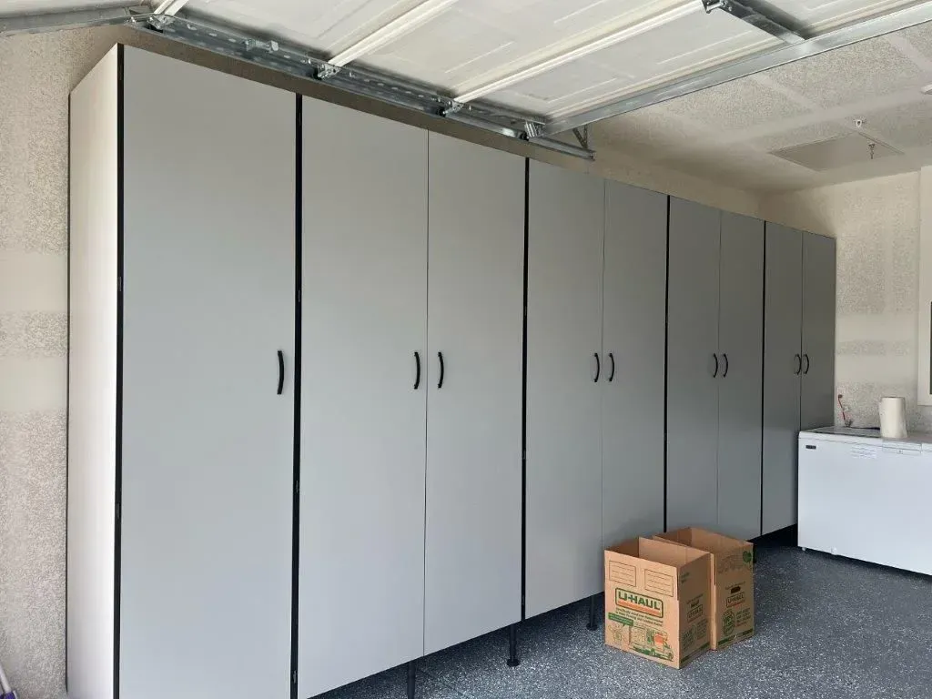 Gray garage cabinets with black trim and handles against a white ceiling and walls. Cardboard boxes sit on the floor.