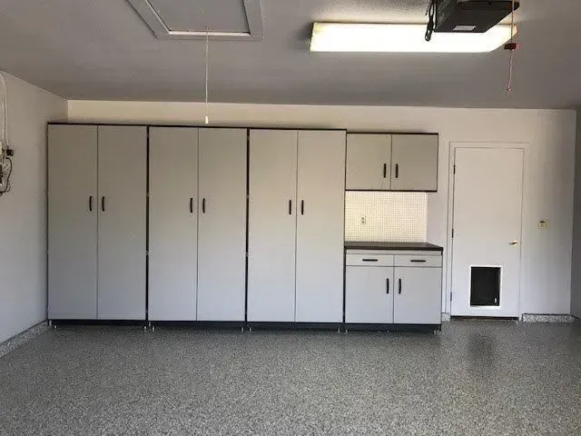 Garage with gray cabinets against a white wall; speckled floor.