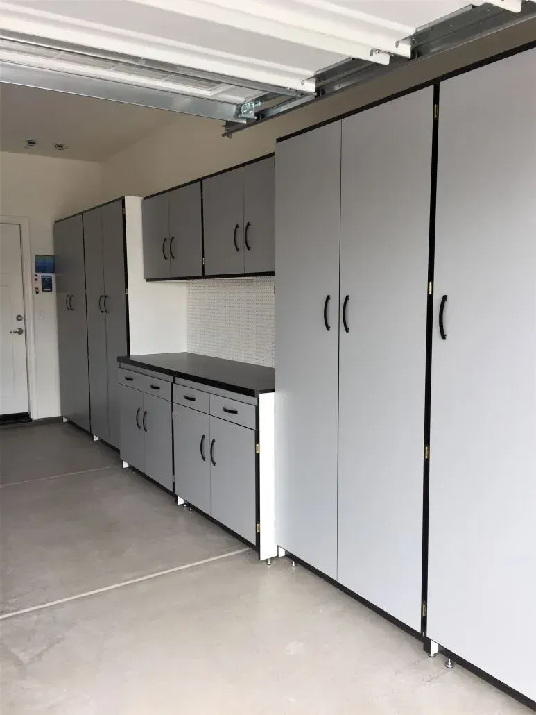 Garage interior with gray storage cabinets along the wall, black countertops, and a white door.