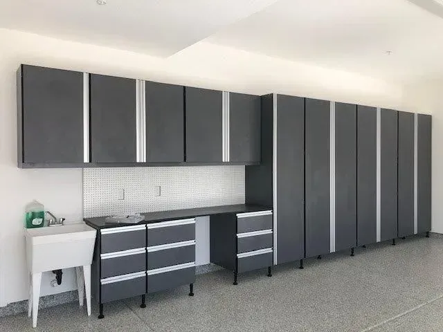 Gray garage cabinets and workbench with sink, against a white wall and speckled floor.