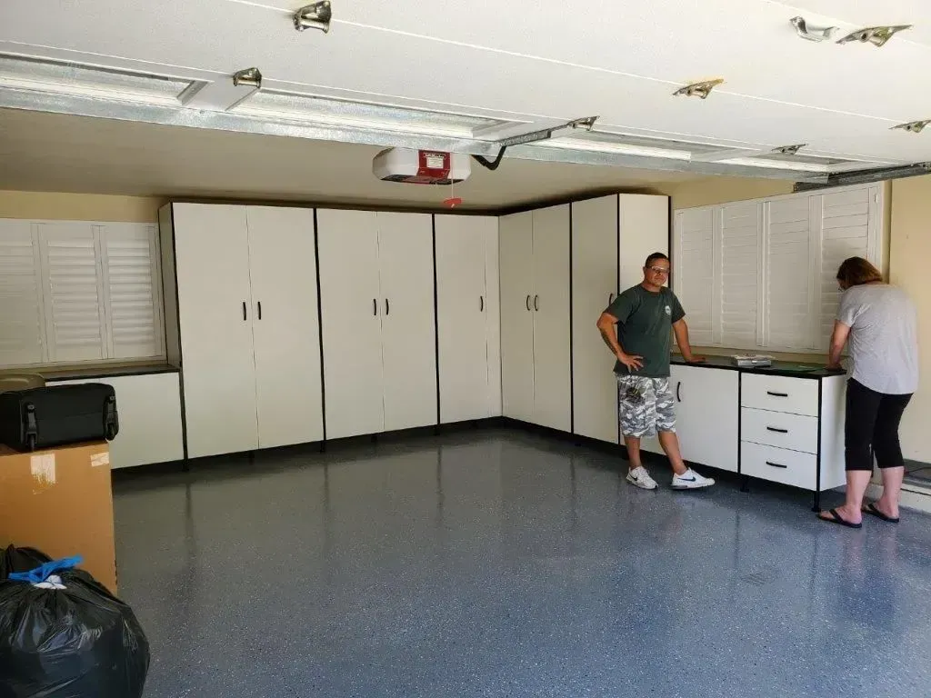A garage with white cabinets and epoxy floor. Two people stand near the cabinets.