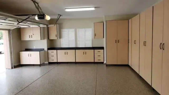 Garage interior with beige cabinets and black countertops. Garage door is open.