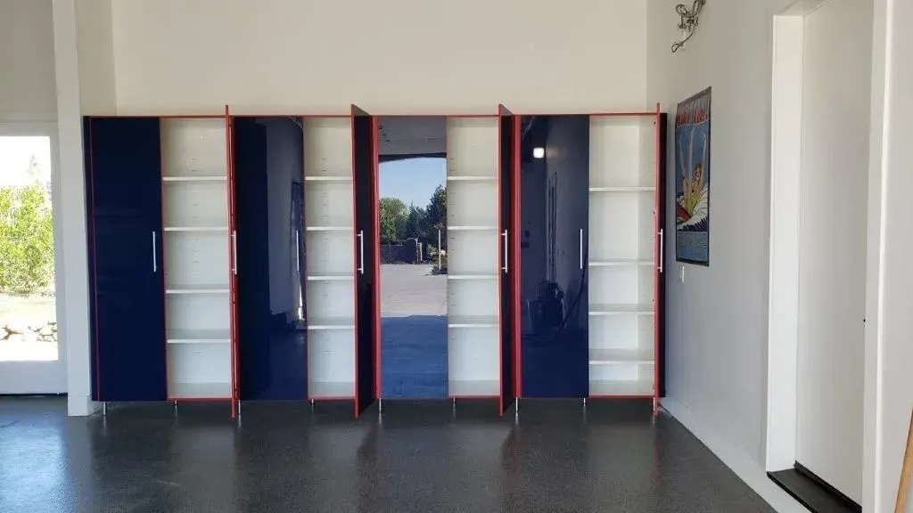 Blue and red storage cabinets with open and closed doors. White interior with shelves, mounted on a garage wall.